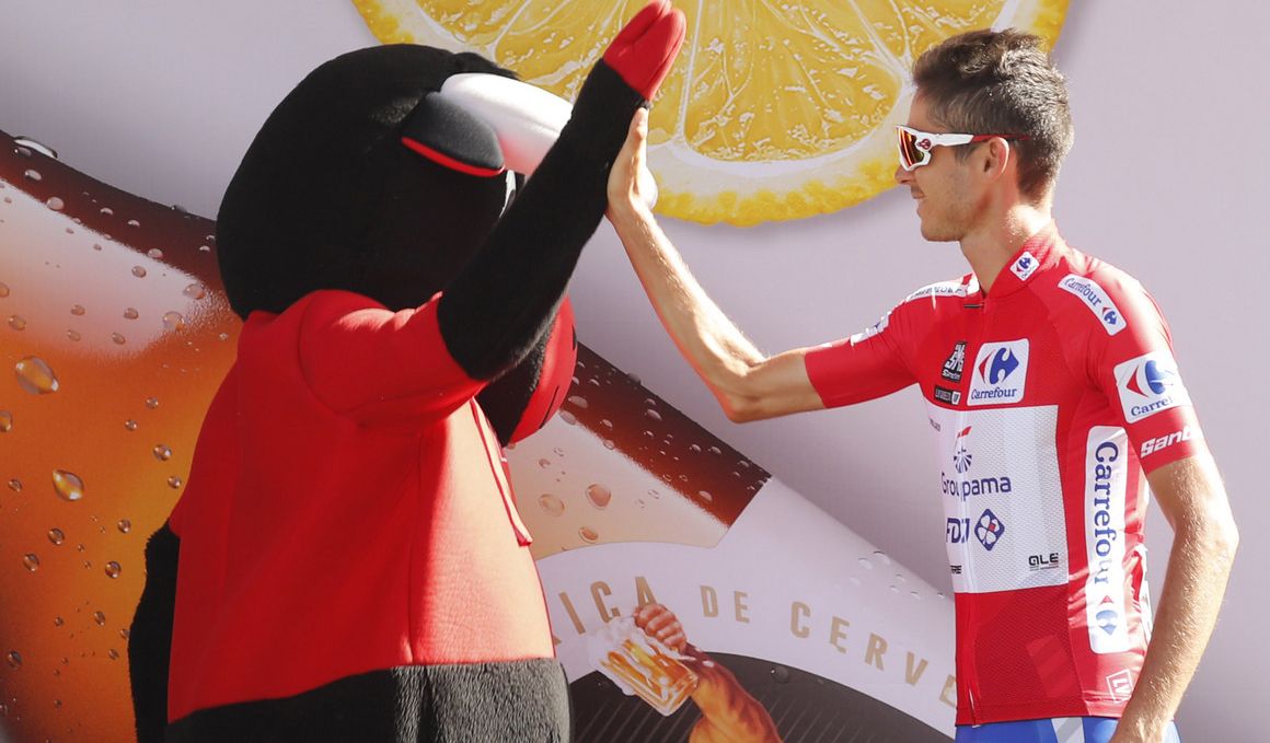 El líder Molard choca sus manos con la mascota de la Vuelta. 