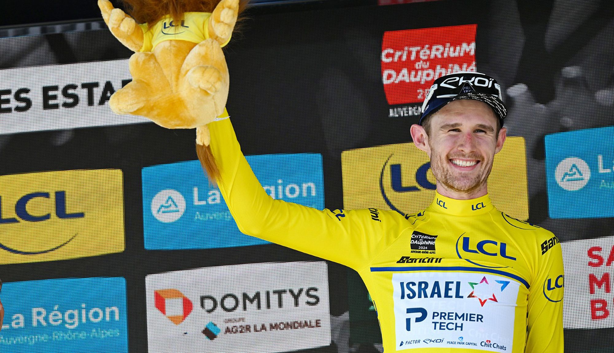 Derek Gee en el podio del Dauphiné vistiendo el maillot amarillo